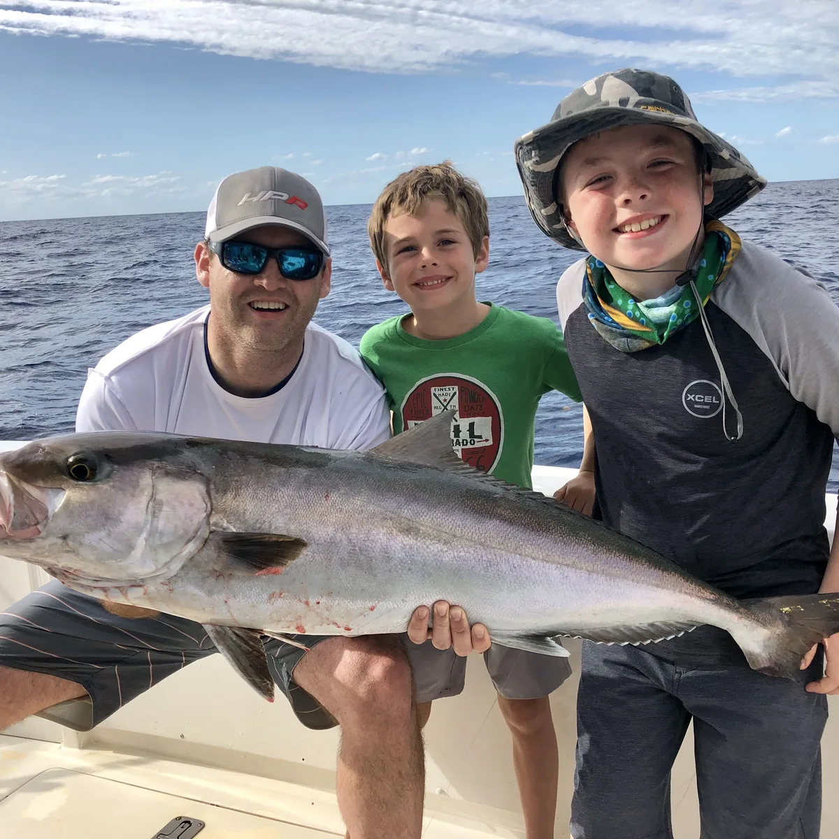A dad and two boys on the deck of Miss Chief, holding a large amberjack