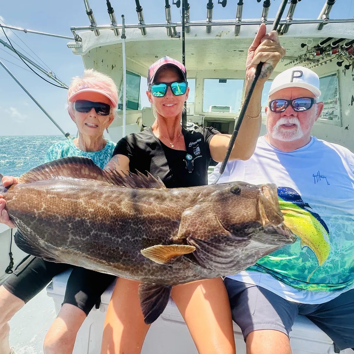 A large grouper held in front of the cabin, with three guests beside it